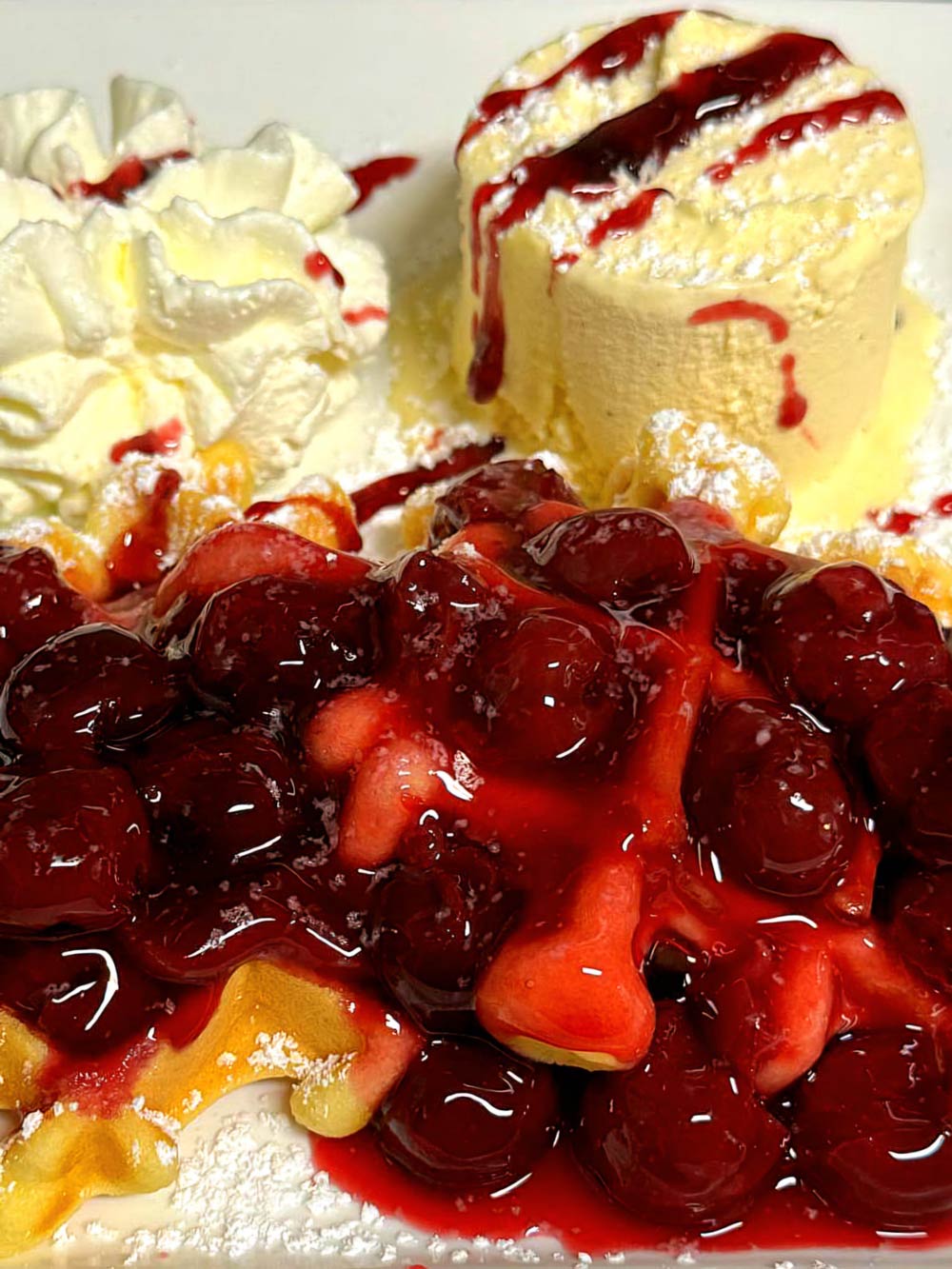 Frische Waffel mit heißen Kirschen, Vanilleeis und Sahne, appetitlich angerichtet