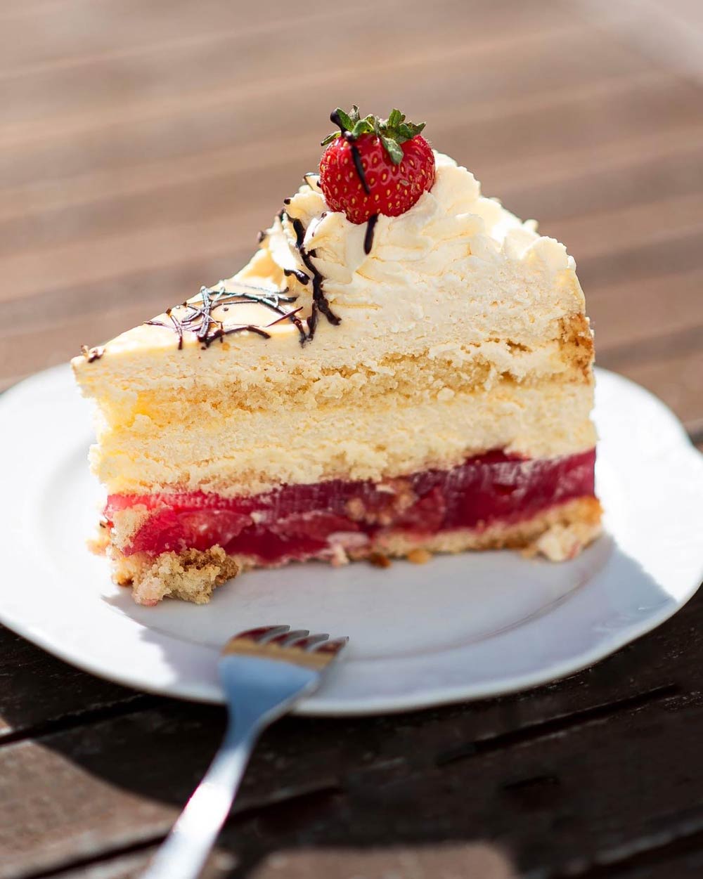 Ein Stück heller Sahnekuchen mit Erdbeerschicht und Schokoraspeln auf weißem Teller