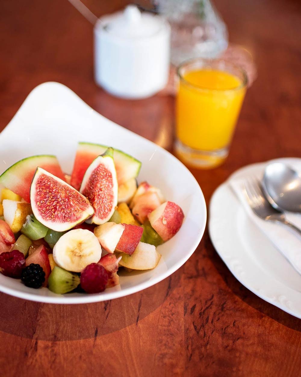 Ein weisser Teller mit frischem Obstsalat und ein Glas Orangensaft auf Holztisch
