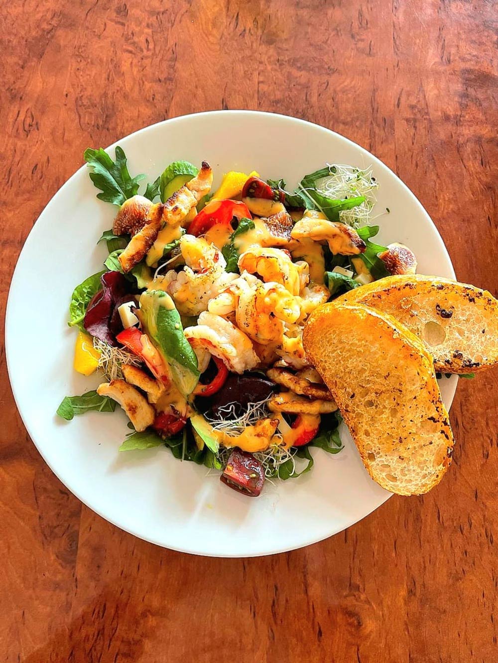 Ein bunter Salatteller mit gebratenem Hähnchenstreifen und zwei gerösteten Brotscheiben